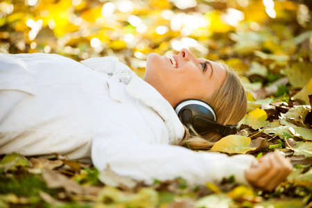 Young happy woman listening music in park in autumnの写真素材