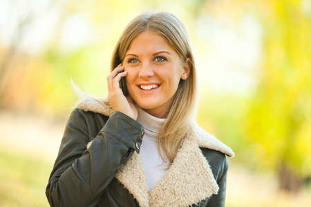 Young happy woman talking on mobile phone in park in autumnの写真素材