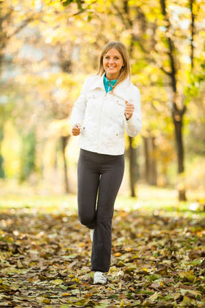 Young happy woman jogging in park in autumnの写真素材