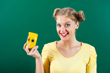 Happy student girl holding photo camera in front of blackboard