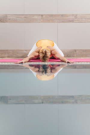 Young woman practicing yoga at swimming pool, Shashankasana Hare poseの写真素材