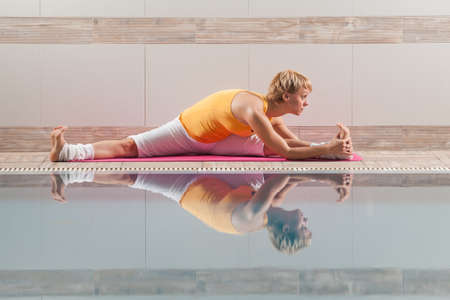 Young woman practicing yoga at swimming pool, Upavistha Konasana Wide Angle Seated Forward Bend poseの写真素材