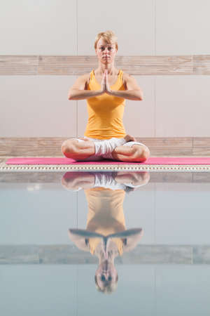 Young woman practicing yoga at swimming pool, Padmasana Half Lotus Positionの写真素材