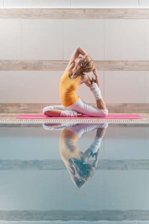 Young woman practicing yoga at swimming pool, Eka pada Rajakapotasana Pigeon poseの写真素材