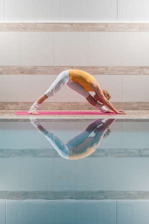 Young woman practicing yoga at swimming pool, Parsvotanasana Intense Side Stretch Poseの写真素材