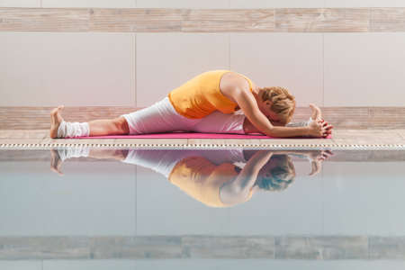 Young woman practicing yoga at swimming pool, Upavistha Konasana Wide Angle Seated Forward Bend poseのeditorial素材