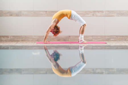 Young woman practicing yoga at swimming pool, Urdhva Dhanurasana Bridge pose