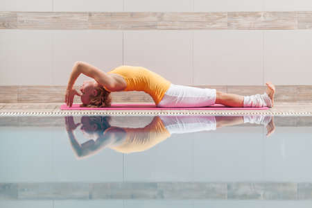 Young woman practicing yoga at swimming pool, Matsyasana Fish poseの写真素材