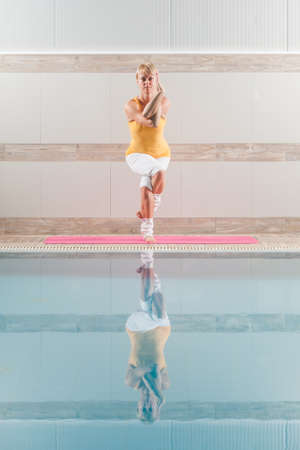 Young woman practicing yoga at swimming pool, Garudasana Eagle poseの写真素材