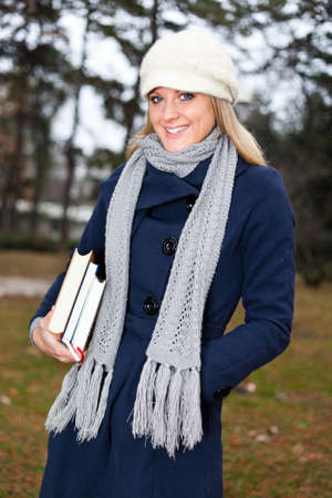 Young happy student girl standing in park with stack of booksの写真素材