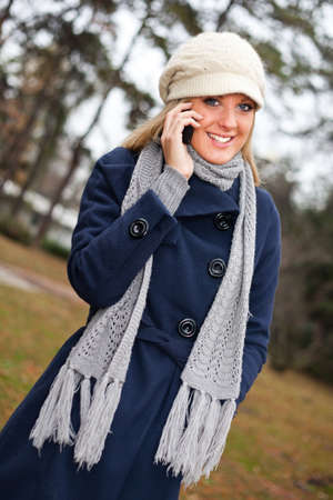 Young happy woman standing in park calling a friend on mobile phoneの写真素材