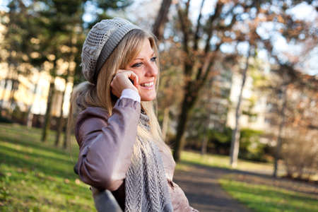 Young woman sitting in park and talking on mobile phoneの写真素材