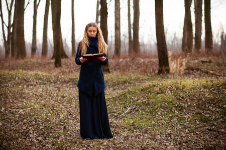 Woman standing lonely in forest in wintertime and reading a bookの写真素材