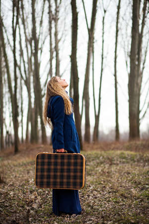 Woman standing in forest with old suitcase looking for a way to goの写真素材