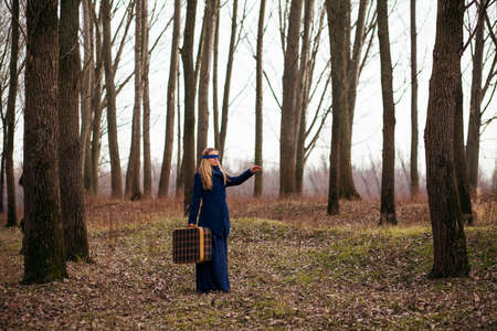 Woman with blindfold walking in forest with old suitcase and looking for a way to goの写真素材