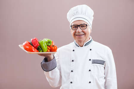 Portrait of happy restaurant's chef in working uniform who is holding vegetablesの写真素材