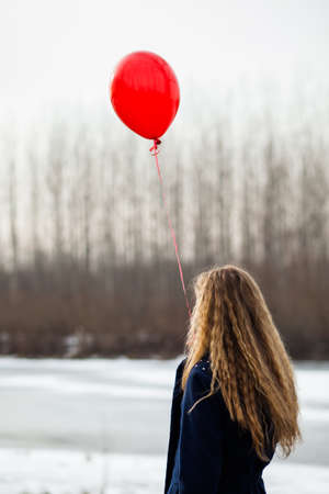 Lonely woman standing near frozen river and holding red balloonの写真素材