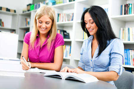 Two happy student girls are learning in library.の写真素材