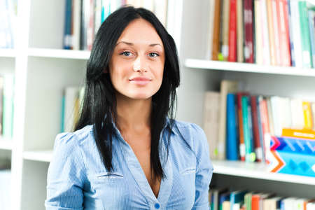Portrait of happy student girl standing in library.の写真素材