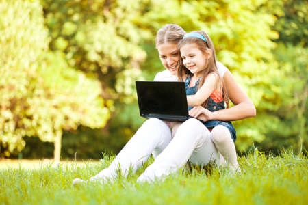 Mother and daughter are having fun in park, they are using laptop.の写真素材