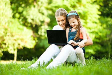 Mother and daughter are having fun in park, they are using laptop.の写真素材