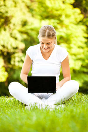 Young happy woman is using laptop in parkの写真素材