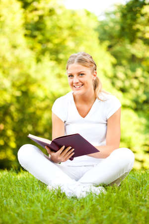 Young happy woman reading book in parkの写真素材