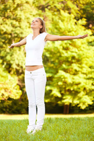 Young happy woman standing in park with arms outstretchedの写真素材