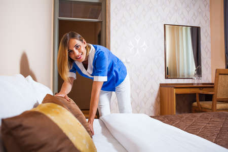 Happy maid is making bed in hotel roomの写真素材