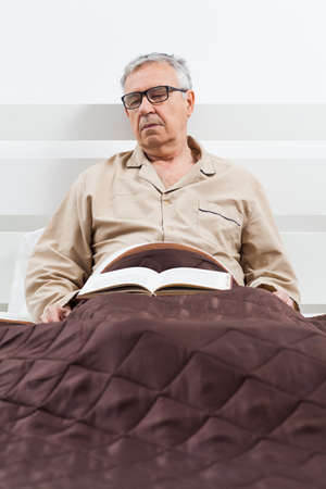 Senior man is lying in bed and he fell asleep while reading a bookの写真素材