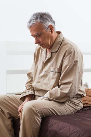 Worried senior is waking up. He is sitting on bed ready to get up.の写真素材