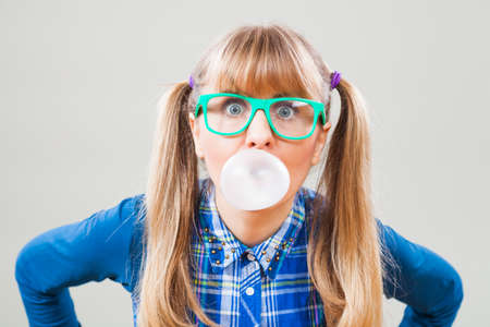 Studio shot portrait of nerdy woman who is blowing bubble gum.