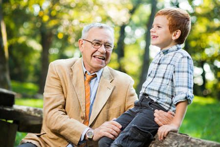 Grandfather and grandson are sitting and talking in parkの写真素材