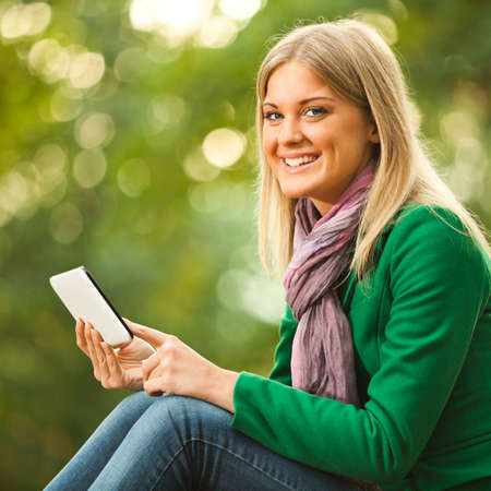 Happy woman is using digital tablet in park.の写真素材