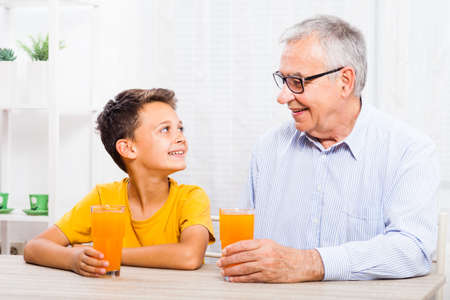 Grandfather and grandson are drinking orange juice at home. Healthy lifestyle.の写真素材