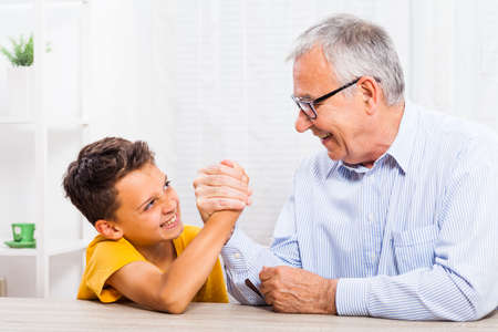 Grandfather and grandson arm wrestle at home.の写真素材