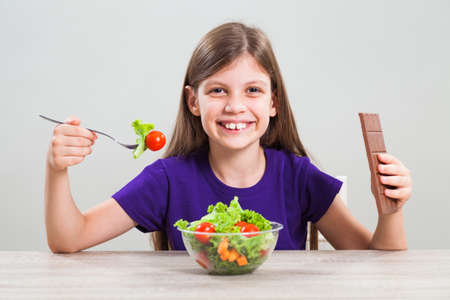 Little girl likes to eat both chocolate and salad.の写真素材