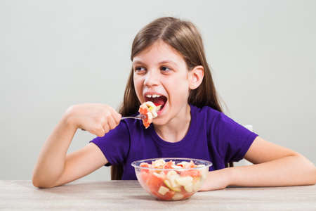 Happy little girl is eating fruit salad.の写真素材