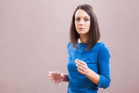 Portrait of young woman who is taking a pill because of illness.の写真素材
