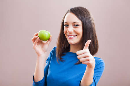 Young woman is holding an apple and smiling.の写真素材