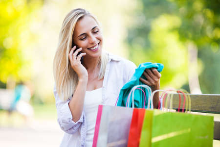 Young happy woman sitting in park after shopping and calling to a friend.の写真素材