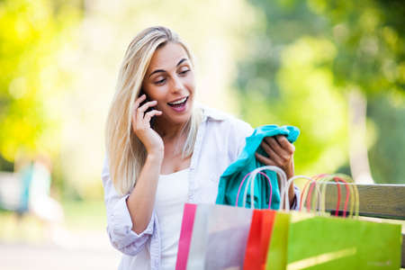 Young happy woman sitting in park after shopping and calling to a friend.の写真素材