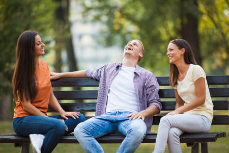 Three friends are sitting on bench in park and talking.の写真素材