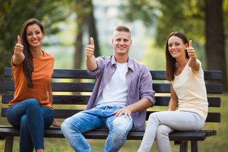 Three friends are sitting on bench in park and talking.の写真素材