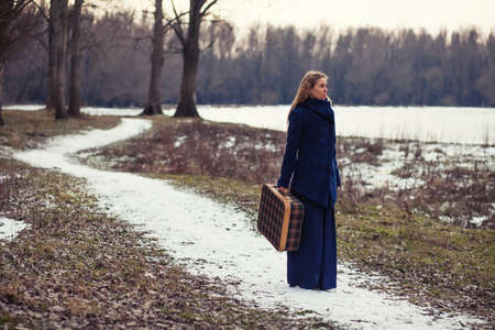 Woman walking in forest with old suitcase in wintertime. Image is intentionally toned.の写真素材