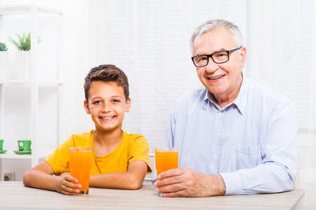 Grandfather and grandson are drinking orange juice at home. Healthy lifestyle.の写真素材