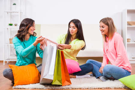 Three friends are sitting in room with shopping bags and talking.の写真素材