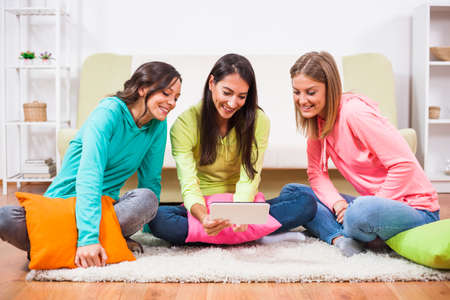 Three friends are sitting in room and using digital tablet.の写真素材