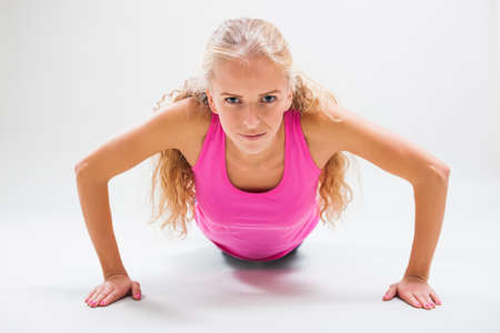 Studio shot image of young woman who is doing push-ups.