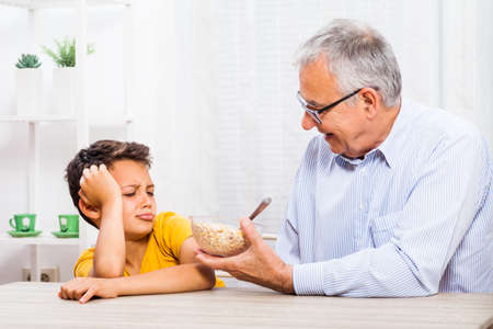 Grandfather is giving oatmeal to his grandson but he refuses to eat it.の写真素材